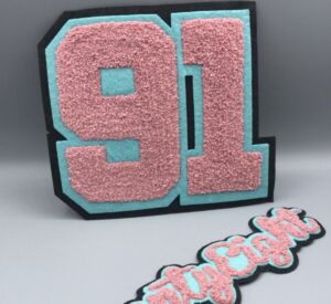 a set of two big chenille embroidered big patches; on white studio background; the top 91 number double felt black and cyan felt and baby pink fluffy embroidered; the bottom text alphabet show half of the patch reads ty eight on the same pattern and styling.