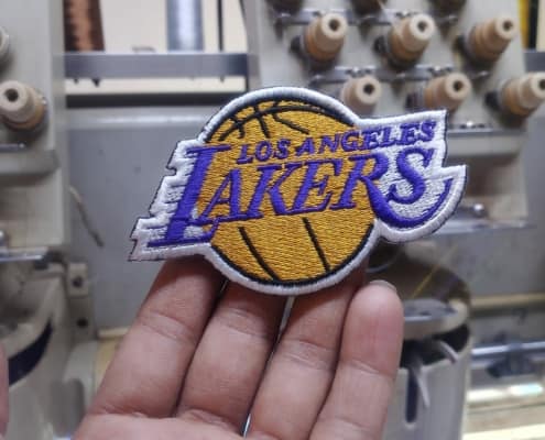 hand holding los angeles lakers official logo as embroidery patch front of an embroidery machine inside factory. 