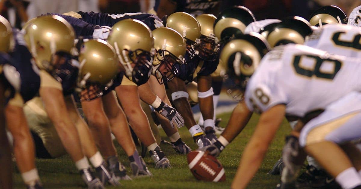 american football players lean heads to heads for ball showing players numbers on jerseys on shoulders and back