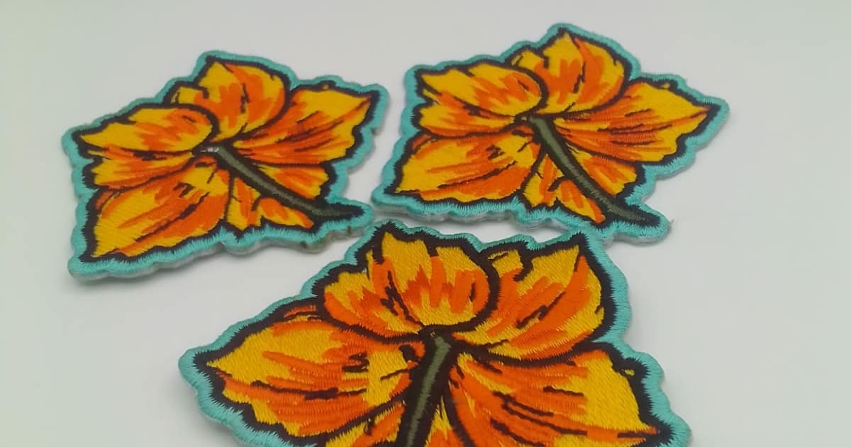three clover flower embroidery patches in yellow and orange thread with sea green embroidered trim on photographed on white studio background