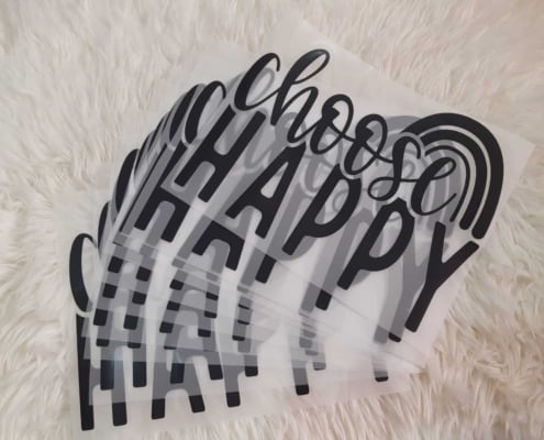 transparent heat transfer direct to film plastic films for a text printing on clothing says "CHOOSE" in stylish font on top and flat text "HAPPY" in blank ink