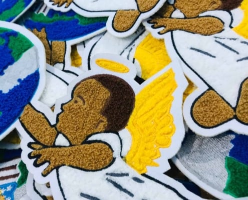 bulk chenille embroidered large patches show an artwork of two angle babies side by side wearing white top, yellow wings and holding a globe over the head showing U.S flat burning