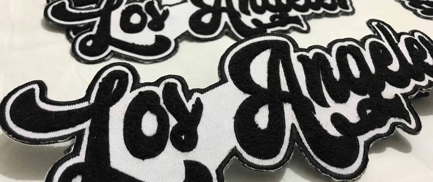  a set of five 10 inches wide chenille embroidered made custom script patches that say LOS ANGELES in black yarn on white scrim felt. The four patches lay down to the floor while the fifth shows off front of white background studio. Featuring black embroidered outline on white fabric and beautiful curve font fluffy city name of great California. 