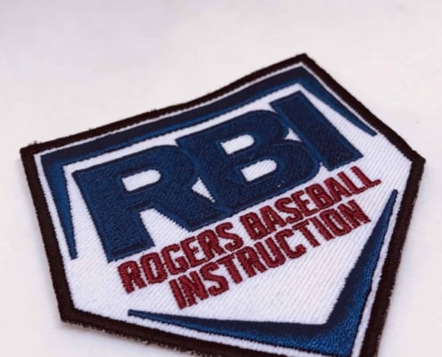red threaded rogers basketball instruction monogram in shield shape die cut embroidery in black edge, whit fabric, navy blue text of RBI