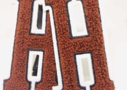 6" tall H chenille patches on white fabric and black embroidery border