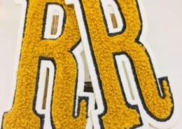 a set of letter R in studio background on white backer fabric, black edge and gold yellow frizzy yarn