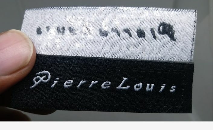 human hand from left hold custom label for Pierre Louis front and back to show iron on glue