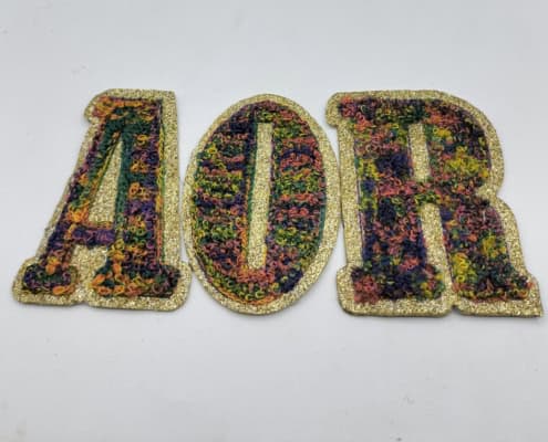 a white studio plain background show three glitter based multi color chenille embroidered letters A O R respectively