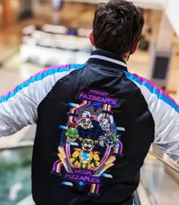 boy opening arms in open area shows his back wearing two tone varsity jacket in black back and white sleeves and big custom design on the back