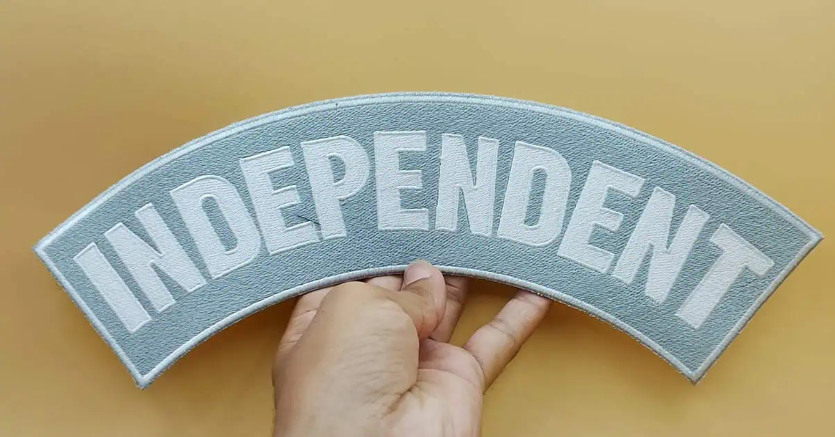 a human hand shows big back patch for independent biker rule embroidered on grey fill stitch and white text inside studio