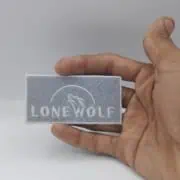 human hand from the right side of frame hold 3 inches wide embroidered patch for lone wolf biker patch on grey filled stitch on the back and white text and lone face on the top inside the studio 
