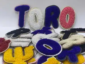 2.5" tall multi color english alphabet and greek chenille letter patches spread over to each other; all on different colors of glitter sheet